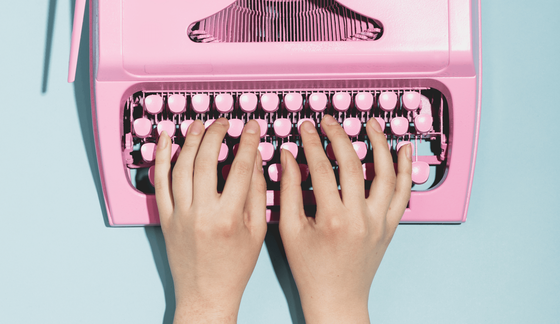 Hände auf einer pinken Schreibmaschine.