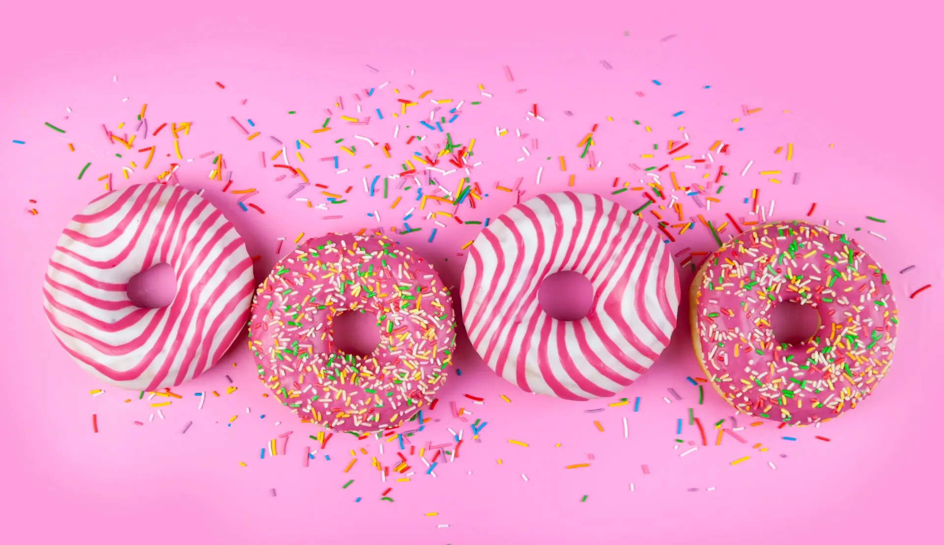 Vier pinke Donuts mit bunten Streuseln als Symbolbild für den Vergleich von drei Homepage-Baukästen